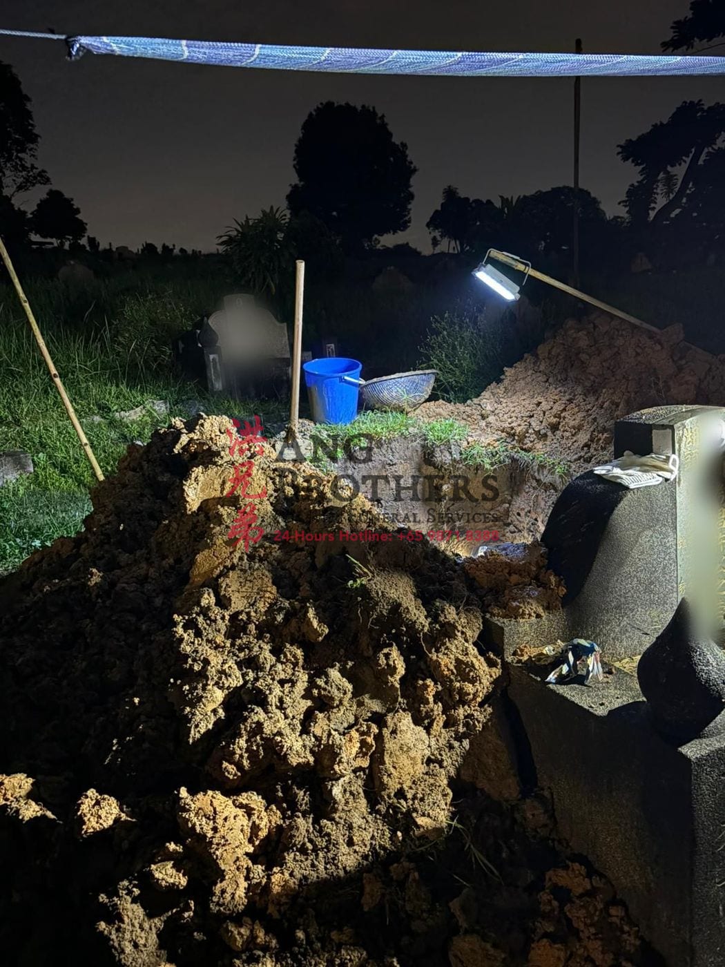 A grave exhumation carried out with care under lamplight by Ang Brothers