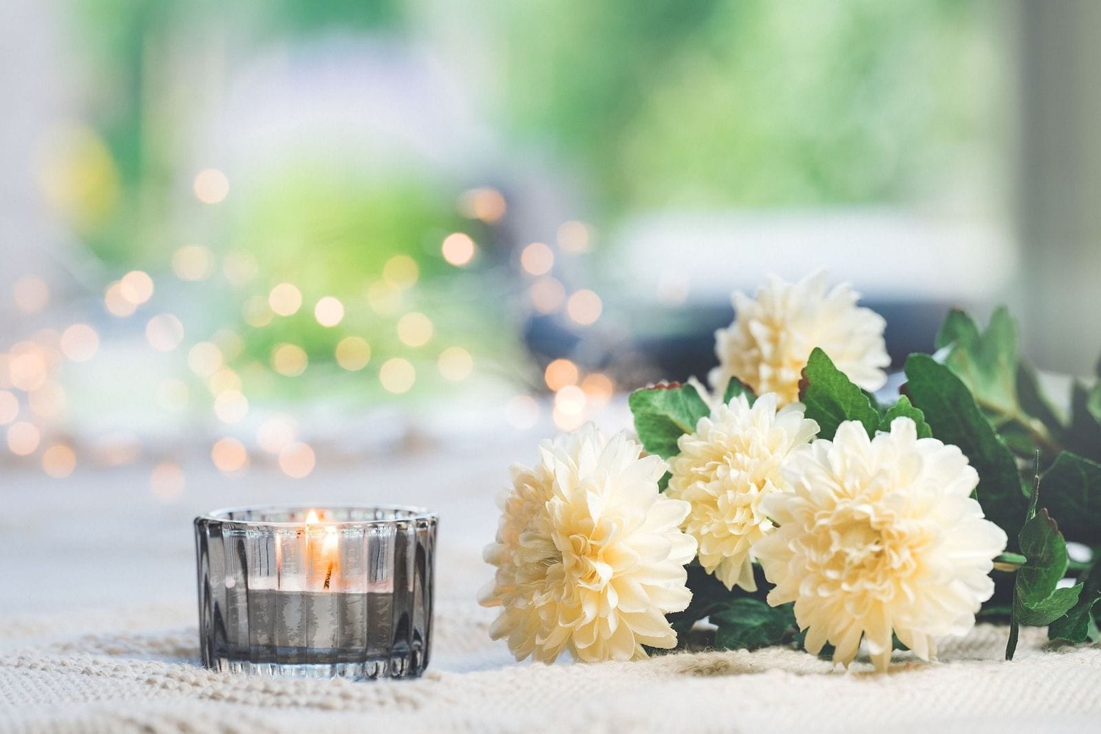 A lit candle beside white tribute flowers